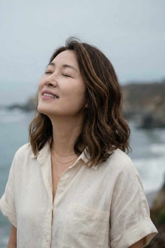 Wavy lob haircut at collarbone length
on a woman over 50 with an oval face,
Pacific coast morning light